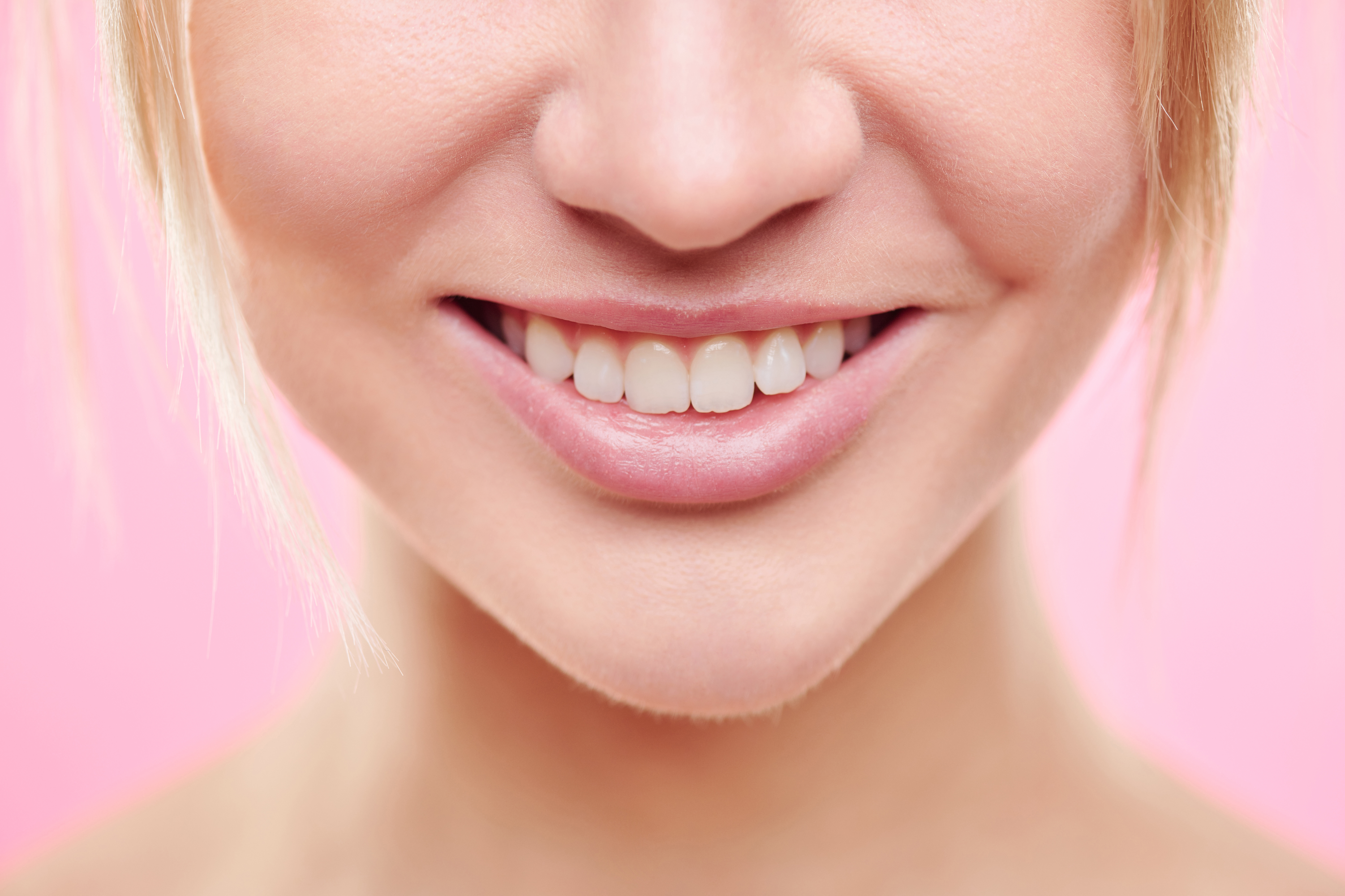 Close-up of lower part of face of young healthy female with toothy smile and natural makeup in isolation